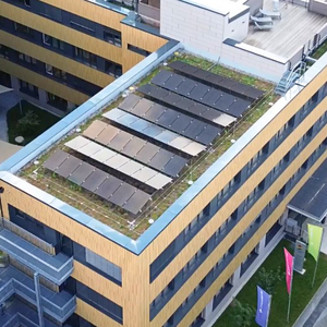 Luftaufnahme des modernen Verwaltungsgebäudes der Stadtwerke Hof in Hof, Bayern, mit grünen Solarpaneelen auf dem Flachdach, umgeben von Bäumen, Parkplätzen und einer asphaltierten Straße – Symbol für nachhaltige Energie und Einspeisemanagement.