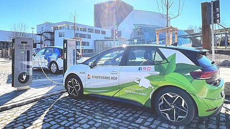 Zwei E-Autos mit Beklebung der Stadtwerke Hof stehen an Ladestationen vor dem Theater Hof.