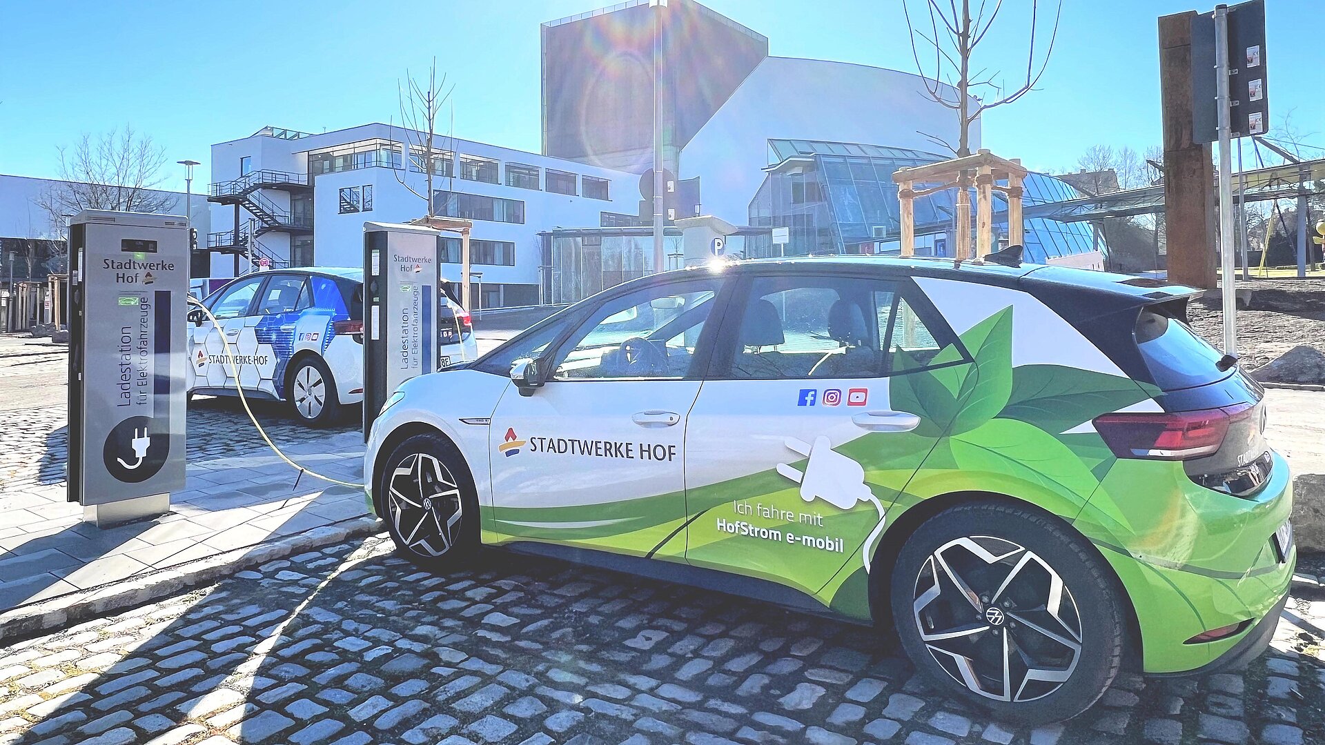 Zwei E-Autos mit Beklebung der Stadtwerke Hof stehen an Ladestationen vor dem Theater Hof.